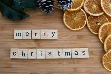 merry christmas text on wooden tiles with holly, dried oranges and pine cones border, isolated on wooden background