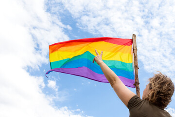 Unrecognizable woman waving a rainbow flag. Raising two fingers in victory