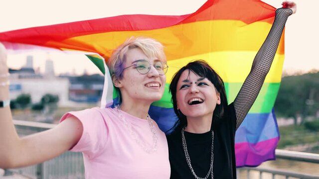 Portrait of happy non-binary couple waving rainbow flag
