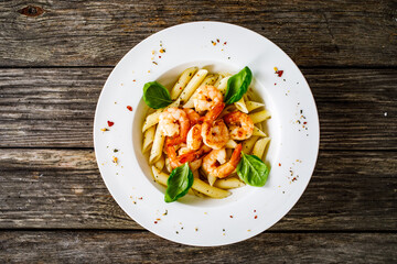 Penne with fried prawns on wooden background
