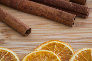 Dried slices of orange in the foreground and cinnamon sticks in the background on wooden background
