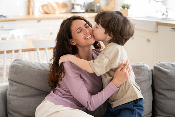 Small boy give mom tender kiss in cheek embracing single parent mum on mother day or greeting with...