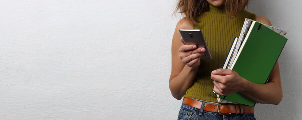 Woman holding pile of notebooks and using smartphone.Empty wahite space