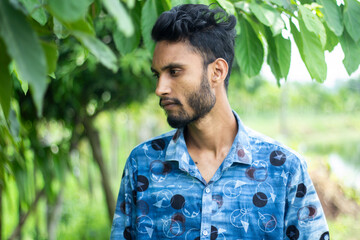 A young man is standing in style wearing a blue dress and his short beard and his behind background...