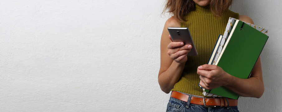 Woman holding pile of notebooks and using smartphone.Empty wahite space