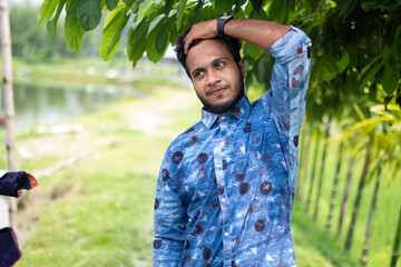 A young man is standing in style wearing a blue dress and his short beard and his behind background...