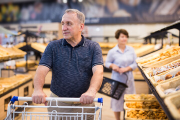 mature man choosing bread and baking in grocery section of supermarket