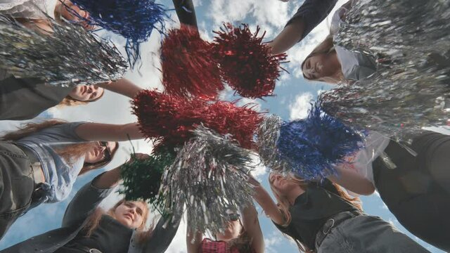 Cheerful girls in the meadow waving multi-colored cheerleading pompoms.