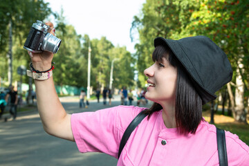 Fototapeta premium A young girl with a camera makes a selfie in a city park.