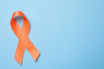 Orange ribbon on light blue background, top view with space for text. Multiple sclerosis awareness