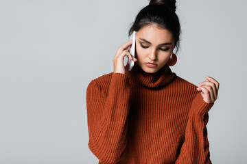 Fototapeta premium young woman in knitted sweater talking on smartphone isolated on grey