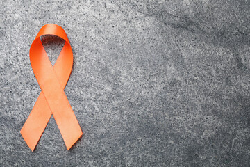 Orange ribbon on grey table, top view with space for text. Multiple sclerosis awareness