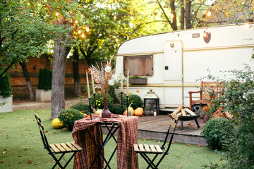 Autumn evening, romantic dinner in the garden. Table with tablecloth and decoration. Trailer with...
