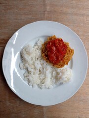 Fried chicken served with chili and tomato sauce on top and also with white rice.