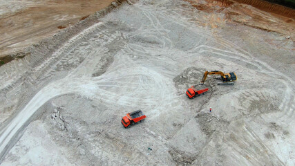 yellow excavator extracts clay and loads into red trucks. Drone view. panorama quarry with blue clay. © drotik