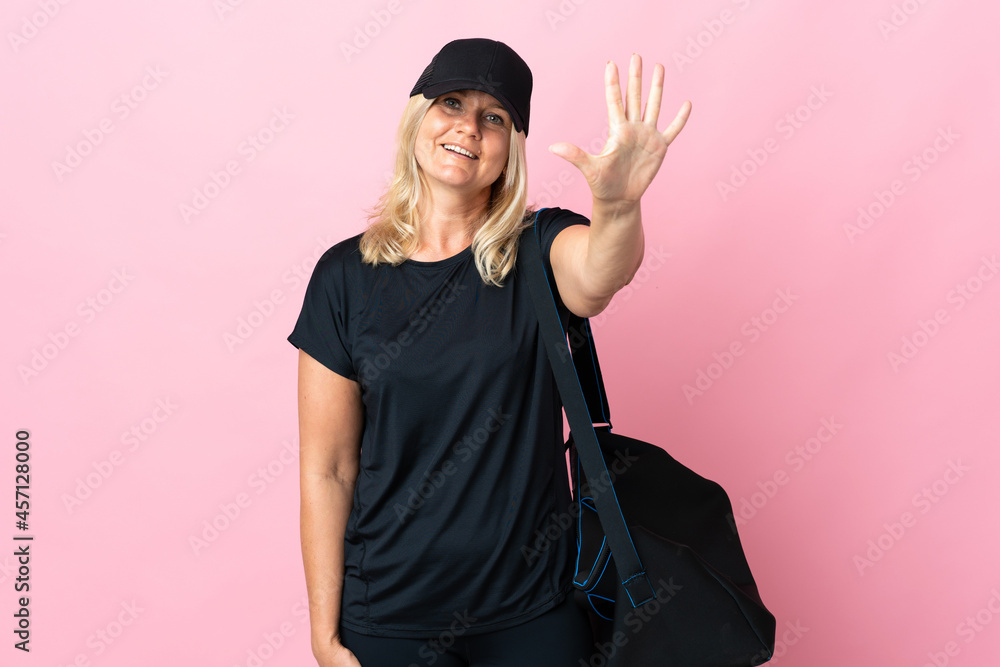 Wall mural Middle age woman with sport bag isolated on pink background counting five with fingers