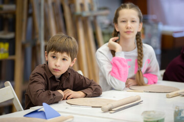 Fototapeta na wymiar A girl and a boy are sitting at a desk in a clay modeling lesson.
