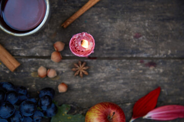 Fototapeta na wymiar Rustic natural cozy still life:candle, fruits, hazelnuts, anise star and cup of tea. Autumn aesthetic concept, red georgine petals. Cozy home with aromatic candle. Thanksgiving Day concept. Copy space