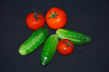 ripe vegetables: green cucumbers and red tomatoes on a black background, the concept of proper and healthy nutrition