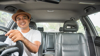 Font view of young asian man with hat driving his car look outside and smiling. - obrazy, fototapety, plakaty