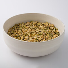 White round plate full of uncooked green lentils. isolated on white