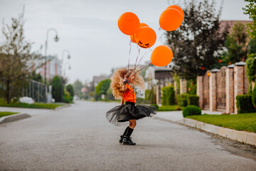 Girl playing on the street with pumpkin balloons while sunrise.