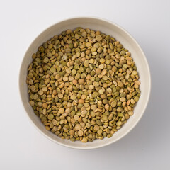 White round plate full of uncooked green lentils. isolated on white. Top view
