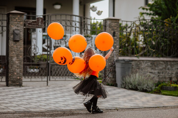 Girl playing on the street with pumpkin balloons while sunrise.
