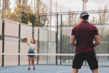 a couple of a boy and a girl playing paddle tennis outdoors.