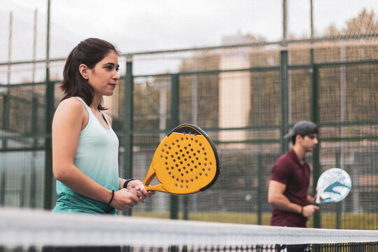 a couple of a boy and a girl playing paddle tennis outdoors.