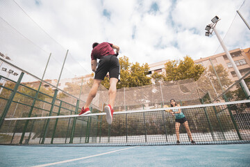 a couple of a boy and a girl playing paddle tennis outdoors.