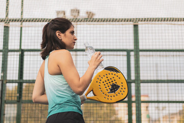 a girl padel player drinking water between the break of the match. - obrazy, fototapety, plakaty