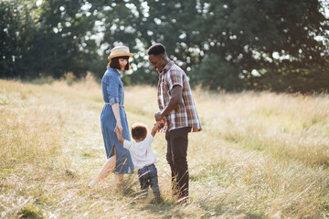 Happy multicultural family of having fun together on fresh air. Caucasian wife and african husband playing with their lovely son on summer field. Unity and values concept.