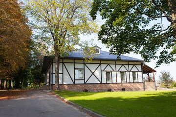 White one-story geman style country house in a picturesque summer or autumn park, half-timbered house, fachwerkhaus.