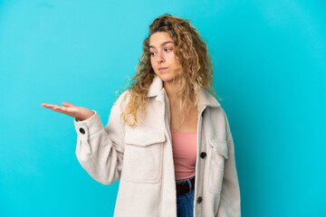 Young blonde woman isolated on blue background holding copyspace with doubts
