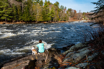 A woman and her dog sitting on a rock at the edge of a fast-moving river