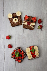Vegetarian whole grain toasts with black currant, strawberry, banana and chocolate veggie paste, funny sandwich for children. Healthy kid food concept. Close-up, selective focus. Top view, flat lay