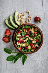 Obraz na płótnie Canvas Healthy veggie salad with avocado, arugula, spinach, strawberries, cashews and seeds- low carbohydrate, low calorie diet. Healthy eating, nutrition and diet concept. Top view, flat lay