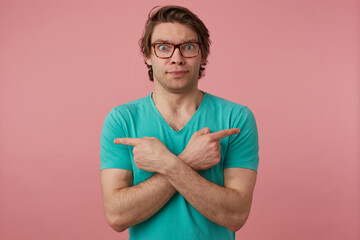 Indoor shot of young brunette male, points with fingers at both sides, can not choose. Isolated...