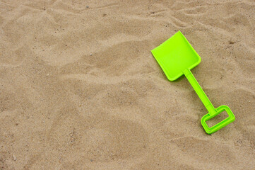 Fototapeta na wymiar bright green plastic toy shovel on background of brown sand with copy space 