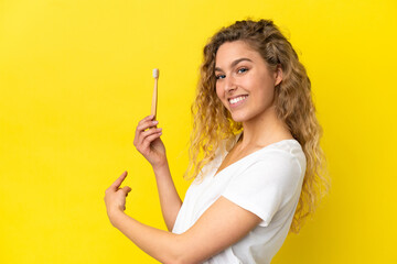 Obraz premium Young caucasian woman holding a brushing teeth isolated on yellow background pointing back