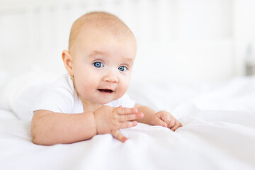 Portrait of cute and smiling four month old baby girl playing on the bed in her room. Happy and dry kid. 