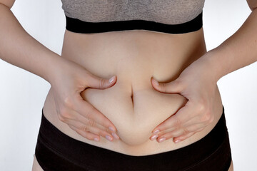 female hands holding a fold of skin on the abdomen, the concept of excess weight, visceral fat,...