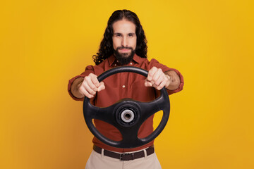 Portrait of serious focused driver guy hold steering wheel look camera on yellow background