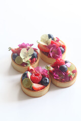 Modern Fruit Tartlets garnished with flowers, on a white background.