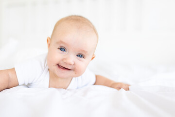 Portrait of cute and smiling four month old baby girl playing on the bed in her room. Happy and dry kid. 