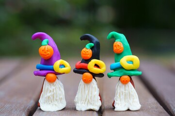 Figures of three dwarfs made of plasticine, decorated with a festive hat and a pumpkin. The concept of Halloween.