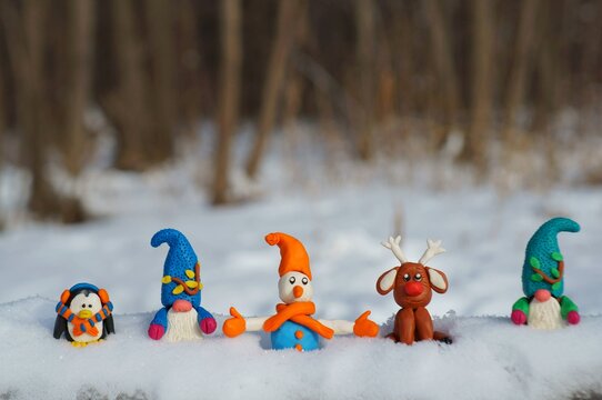 A snowman, a deer, a penguin and two dwarfs in a snowy forest.