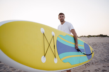 Young man carrying sup board after water surf session