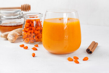 Sea buckthorn smoothie with ginger, honey and cinnamon in the drinking glass on the white table